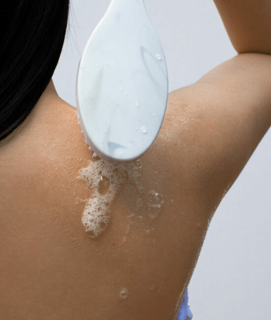 woman lathering soap on back to treat back acne scars
